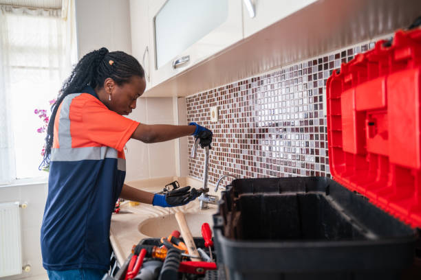 Black female Plumber fixing a leak in the kitchen sink of a house
